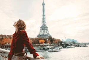 Traveler standing on a bridge over the Seine River with the Eiffel Tower in the background at sunset.
