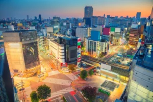 Aerial view of Shibuya at dusk, showcasing the vibrant cityscape with illuminated buildings, busy streets, and the iconic Shibuya Crossing.