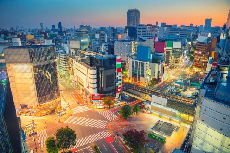 Aerial view of Shibuya at dusk, showcasing the vibrant cityscape with illuminated buildings, busy streets, and the iconic Shibuya Crossing.