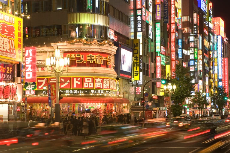 Night view of Shinjuku City with illuminated buildings and bustling street traffic.